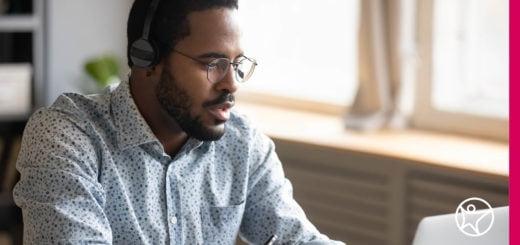 A teacher is wearing headphones and working on a laptop